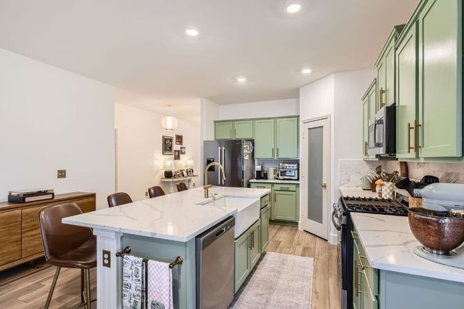Kitchen with green cabinets, appliances with stainless steel finishes, light wood-style flooring, backsplash, and a kitchen bar | Image 12