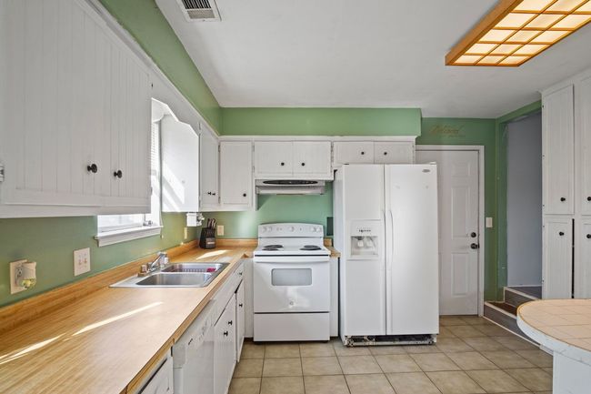 Kitchen featuring white appliances, white cabinetry, light countertops, under cabinet range hood, and light tile patterned floors | Image 7