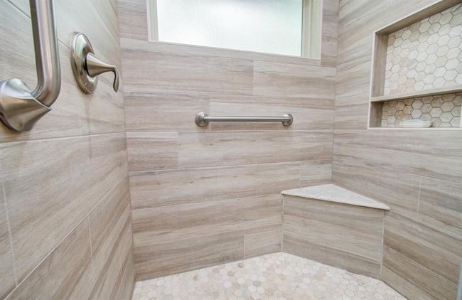 This shower offers a convenient corner seat, custom wall inset, and safety support bars. WOW! | Image 26
