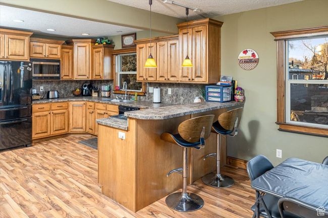 Kitchen featuring pendant lighting, black appliances, kitchen peninsula, a textured ceiling, and light hardwood / wood-style flooring | Image 14