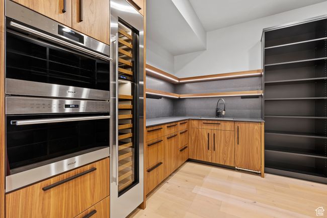Kitchen featuring open shelves, a sink, stainless steel double oven, light wood-type flooring, and modern cabinets | Image 33