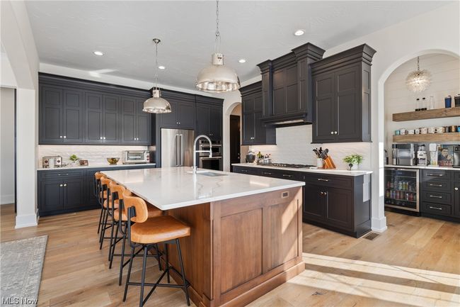 Kitchen featuring beverage cooler, appliances with stainless steel finishes, backsplash, light wood-type flooring, and a center island with sink | Image 11
