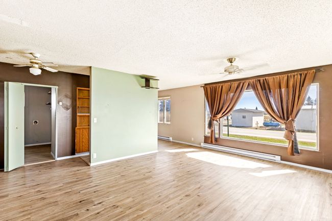 Unfurnished living room featuring a textured ceiling, plenty of natural light, a ceiling fan, and a baseboard heating unit | Image 17