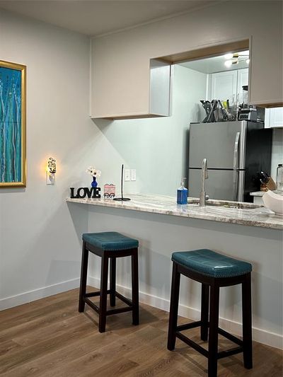 Kitchen featuring kitchen peninsula, a breakfast bar area, dark wood-type flooring, refrigerator, and light stone counters | Image 3