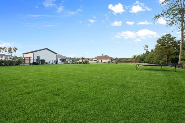 Expansive, lush green yard, bordered by trees. Features a spacious, modern home with a patio, ideal for outdoor activities and relaxation. | Image 48