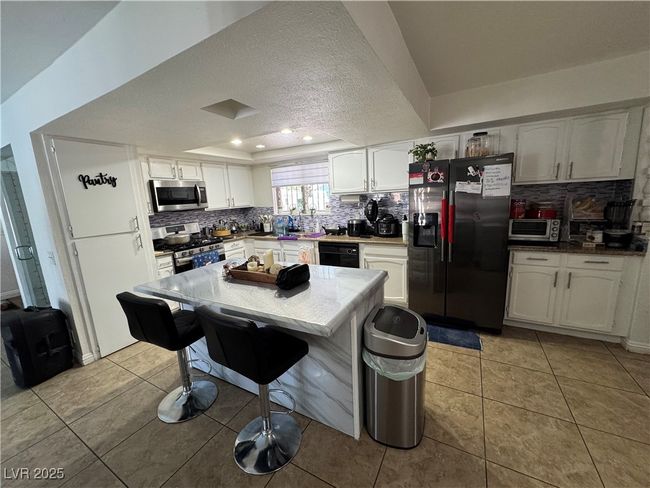 Kitchen with stainless steel appliances, decorative backsplash, a kitchen bar, light tile patterned flooring, and a textured ceiling | Image 4
