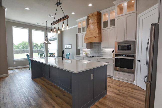 Kitchen featuring custom range hood, stainless steel appliances, backsplash, an island with sink, and pendant lighting | Image 11