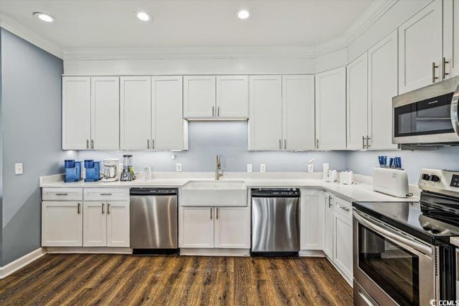 Kitchen featuring appliances with stainless steel finishes, white cabinetry, dark wood-style flooring, ornamental molding, and recessed lighting | Image 9