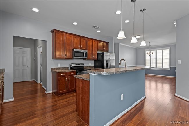 Kitchen featuring stainless steel appliances, dark wood-style flooring, a chandelier, a center island with sink, and pendant lighting | Image 6