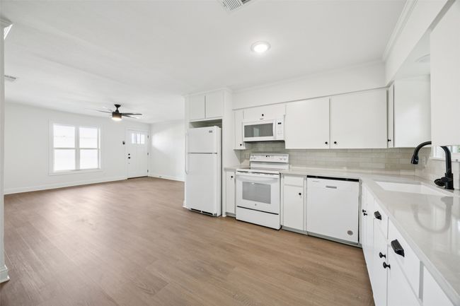 Kitchen featuring white appliances, backsplash, light countertops, a ceiling fan, and white cabinets | Image 8