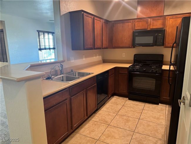 Kitchen with black appliances, light countertops, and light tile patterned floors | Image 8