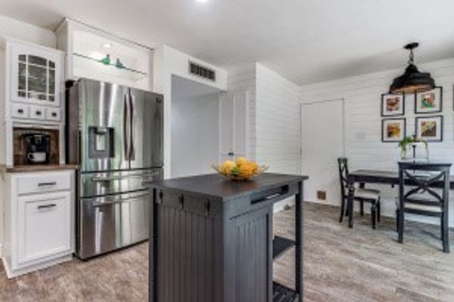 Kitchen with dark countertops, light wood-type flooring, stainless steel fridge, white cabinetry, and visible vents | Image 14