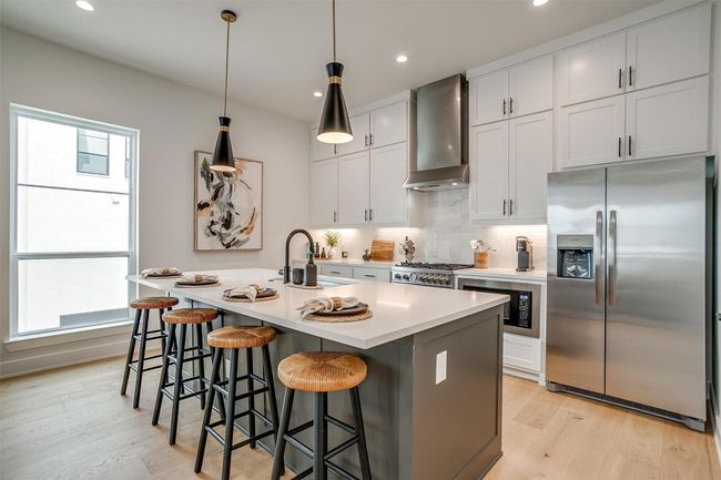 Kitchen featuring light wood finished floors, a sink, decorative backsplash, wall chimney range hood, and appliances with stainless steel finishes | Image 9