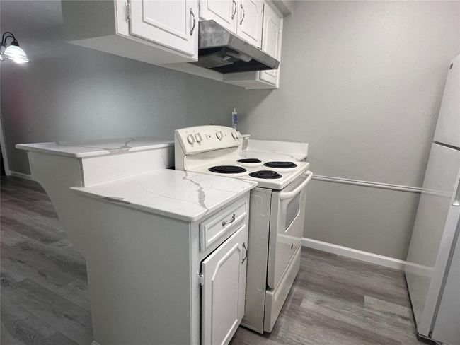 Kitchen with white appliances, under cabinet range hood, dark wood-style floors, and white cabinets | Image 7