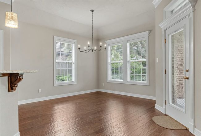 Unfurnished dining area with dark wood-type flooring, a chandelier, and baseboards | Image 10