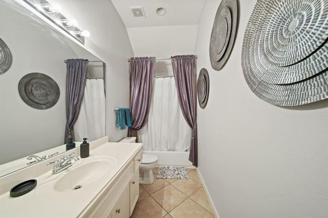 Serving both additional guest bedrooms, this well-appointed bathroom includes a full tub/shower combo, extended vanity, framed mirror, and neutral tile flooring. | Image 41