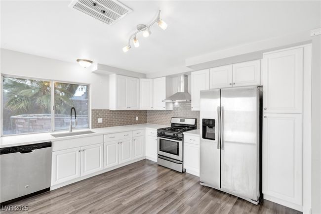 Kitchen featuring a sink, appliances with stainless steel finishes, visible vents, light countertops, and wall chimney exhaust hood | Image 7