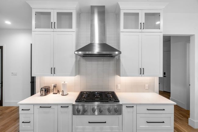 Kitchen with wall chimney range hood, stainless steel gas stovetop, backsplash, light wood-style floors, and white cabinetry | Image 9
