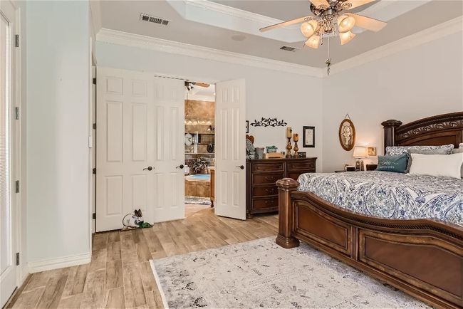 Bedroom featuring visible vents, a raised ceiling, crown molding, and light wood finished floors | Image 19
