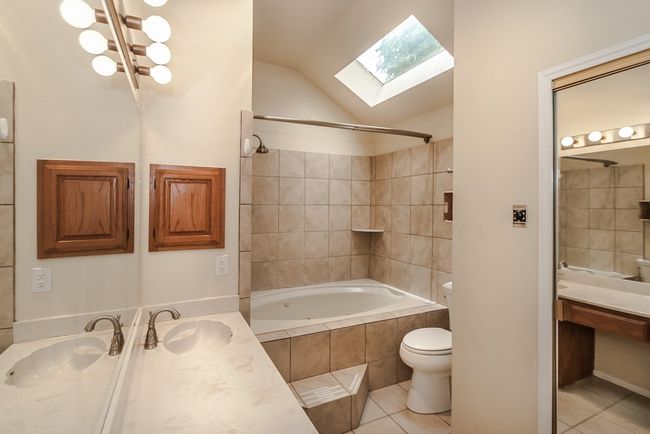 Bathroom with tile patterned floors, a skylight, tiled shower / bath, vanity, and lofted ceiling | Image 12