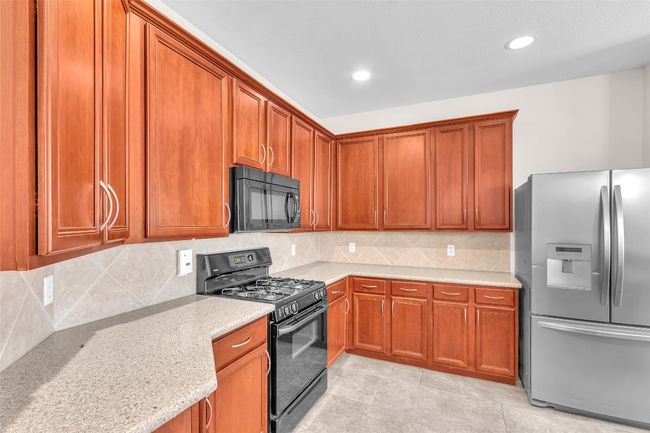 Kitchen with black appliances, light stone counters, tasteful backsplash, recessed lighting, and light tile patterned floors | Image 9