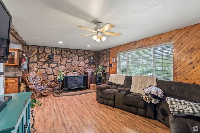 Living area with a wood stove, ceiling fan, wooden walls, a textured ceiling, and wood finished floors | Image 4