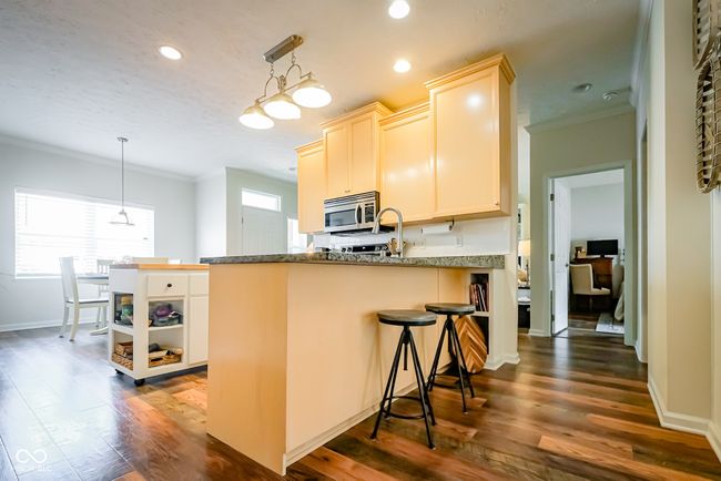 kitchen with stainless steel microwave, crown molding, a peninsula, dark wood-style floors, and baseboards | Image 11