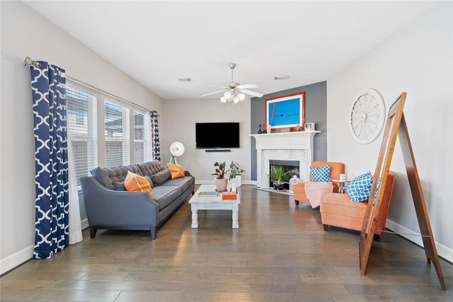 Bright and inviting living room featuring hardwood floors, a cozy fireplace, and stylish decor. The space includes a comfortable sofa, modern accent chairs, and large windows with patterned curtains, allowing plenty of natural light. Perfect for relaxation and entertaining. | Image 21