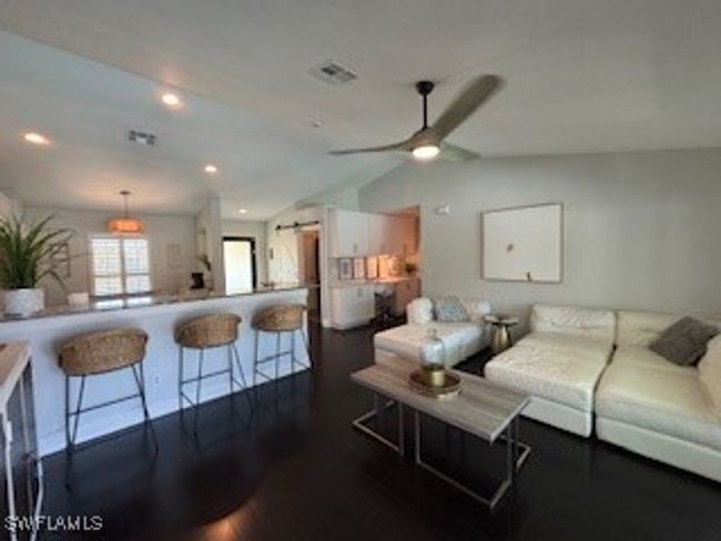 Living room featuring vaulted ceiling, a barn door, dark wood-style floors, visible vents, and ceiling fan | Image 10