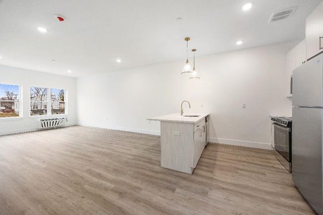 Kitchen with freestanding refrigerator, electric range, a peninsula, a sink, and light wood finished floors | Image 26