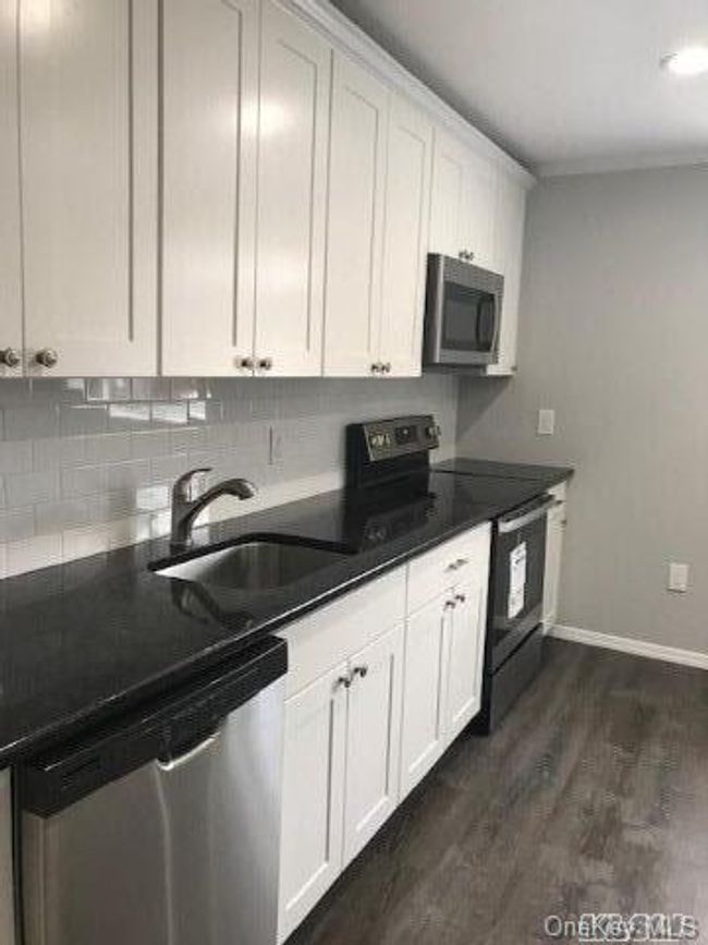 Kitchen featuring dark wood-style floors, a sink, stainless steel appliances, baseboards, and white cabinets | Image 5