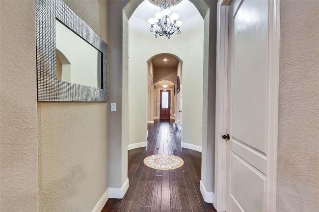 Hall with arched walkways, a textured wall, a chandelier, and hardwood / wood-style floors | Image 16