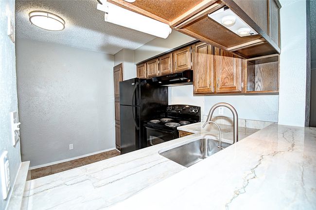 Kitchen with black range with electric cooktop, sink, a textured ceiling, and light stone countertops | Image 16