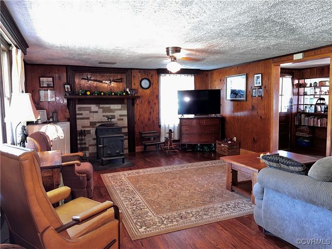 Living room featuring wooden walls, a wood stove, dark hardwood / wood-style flooring, a wealth of natural light, and ceiling fan | Image 23