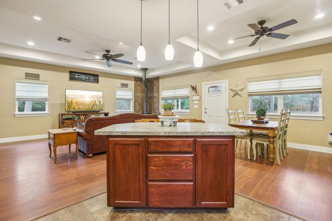 Kitchen featuring a center island, a wood stove, a raised ceiling, pendant lighting, and ceiling fan | Image 16