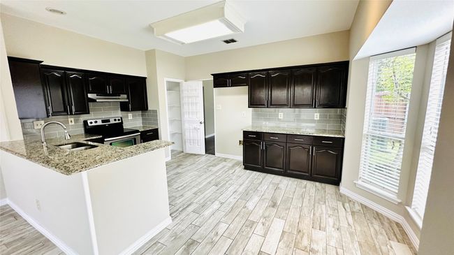 Kitchen with stainless steel range with electric stovetop, light stone countertops, light wood-type flooring, backsplash, and under cabinet range hood | Image 6