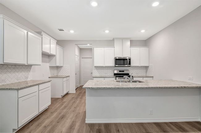 Kitchen with appliances with stainless steel finishes, light stone countertops, white cabinetry, backsplash, and light wood finished floors | Image 8