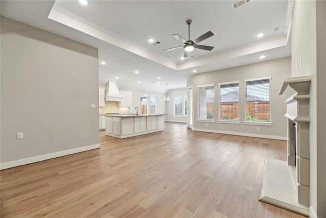 The open-concept layout connects the family room, kitchen, and dining area seamlessly, highlighted by an elegant tray ceiling, warm LVP flooring, and a wall of windows that fill the space with natural light. A romantic gas-log fireplace anchors the room, while the oversized island invites gathering and everyday comfort. | Image 8