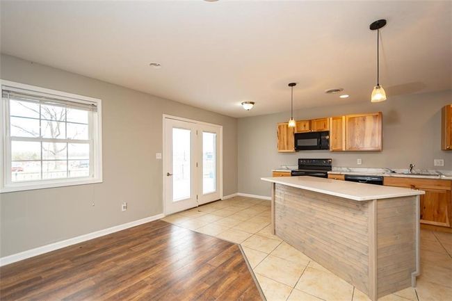 Kitchen with baseboards, hanging light fixtures, black appliances, light countertops, and a center island | Image 9