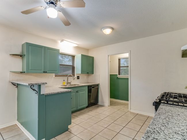 Kitchen featuring black dishwasher, light tile patterned flooring, open shelves, range with gas stovetop, and green cabinets | Image 12
