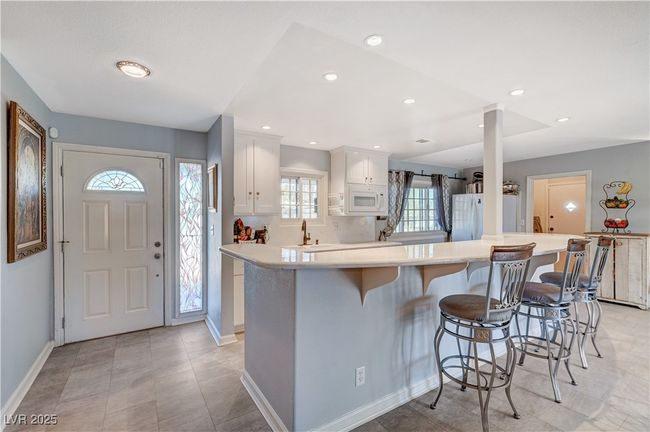 Kitchen with white appliances, white cabinetry, a breakfast bar, light countertops, and baseboards | Image 55