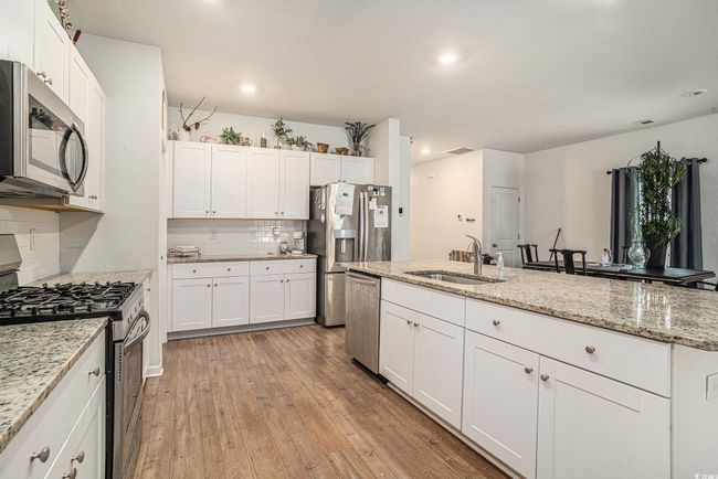 Kitchen with appliances with stainless steel finishes, a sink, decorative backsplash, light wood-style floors, and white cabinets | Image 13