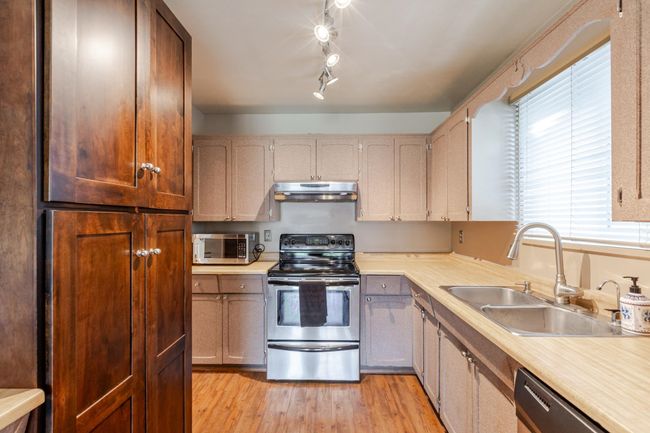 Kitchen featuring light countertops, under cabinet range hood, a sink, light wood-style flooring, and appliances with stainless steel finishes | Image 17