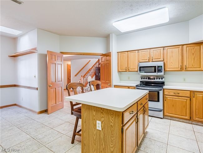 Kitchen with a textured ceiling, brown cabinets, light countertops, electric stove, light tile floors, and a center island | Image 17