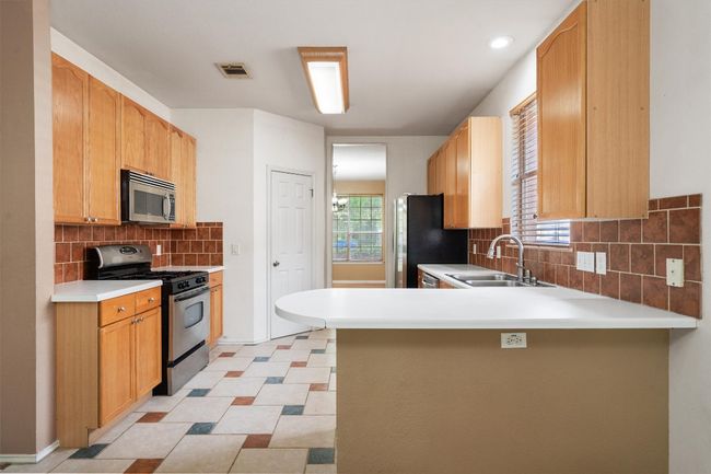 Kitchen featuring stainless steel appliances, a sink, a peninsula, backsplash, and light countertops | Image 16