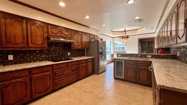 Kitchen featuring stainless steel refrigerator with ice dispenser, wine cooler, under cabinet range hood, black electric cooktop, and ornamental molding | Image 6