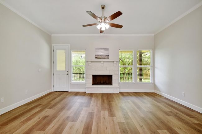 Unfurnished living room featuring a fireplace with raised hearth, crown molding, wood finished floors, and ceiling fan | Image 4