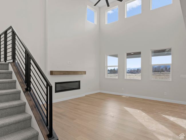 Unfurnished living room featuring a high ceiling, a ceiling fan, baseboards, light wood-style floors, and a glass covered fireplace | Image 6