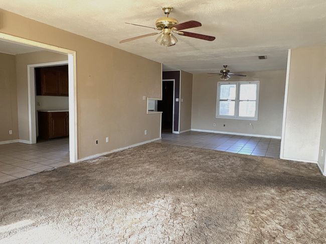 Unfurnished living room with a textured ceiling, carpet, a ceiling fan, and tile patterned flooring | Image 11