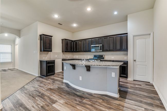 Kitchen with stainless steel appliances, a kitchen island with sink, dark wood-type flooring, light stone countertops, and decorative backsplash | Image 10
